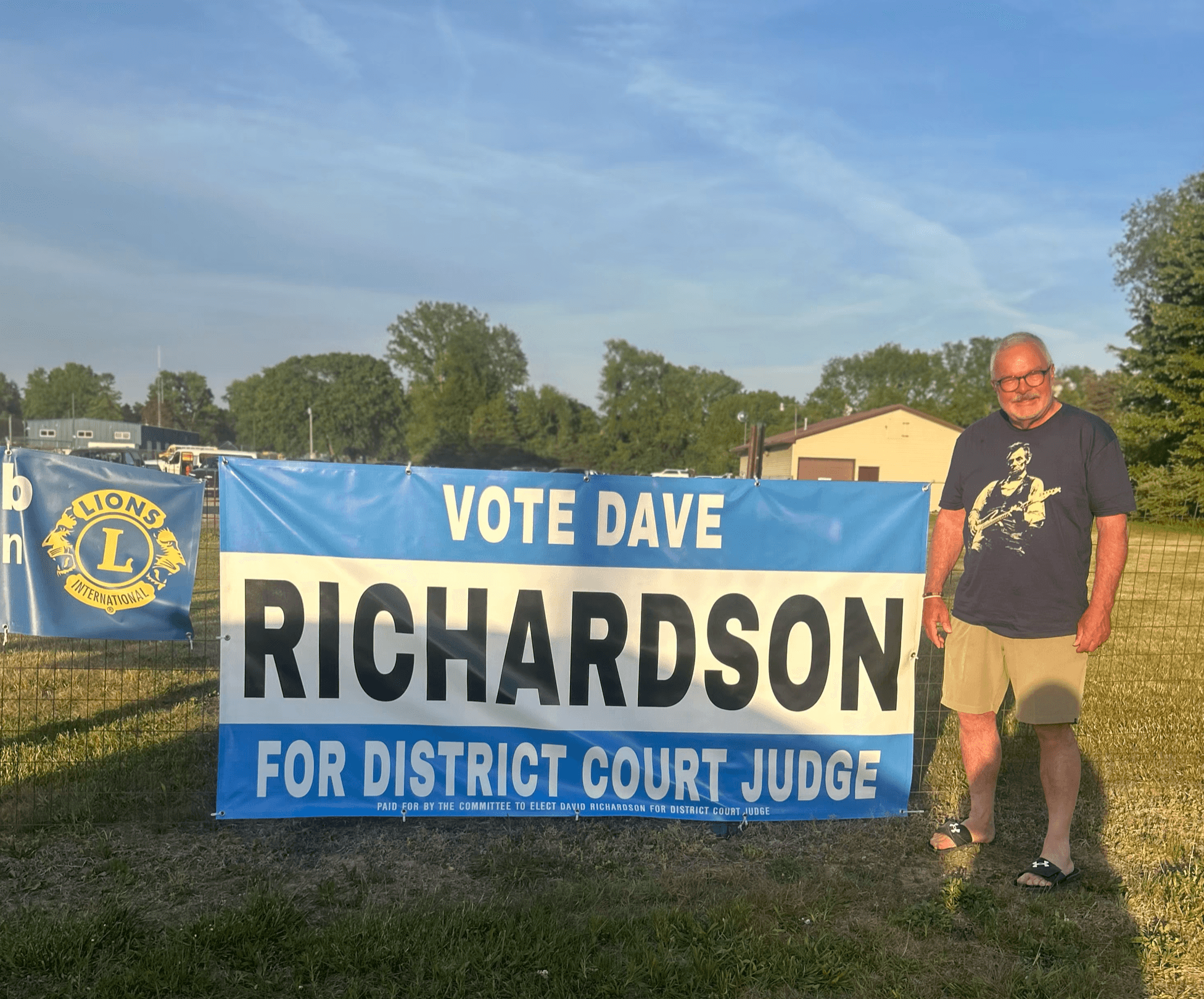 Dave Richardson standing by a campaign yard sign